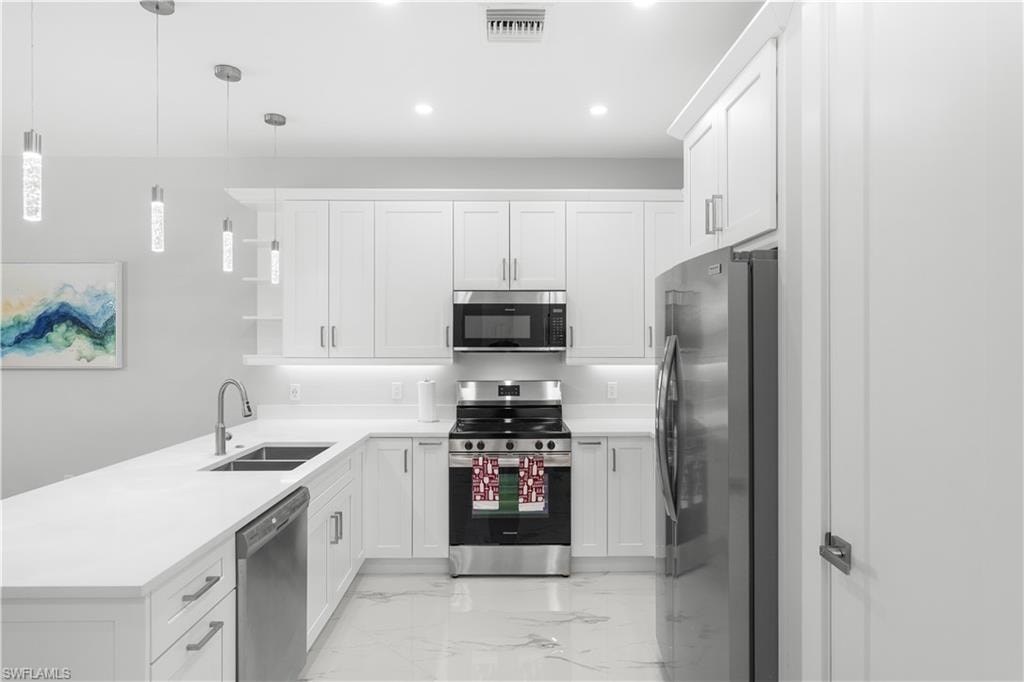 Modern kitchen with white shaker cabinetry, stainless steel appliances, white countertops, and contemporary pendant lighting fixtures
