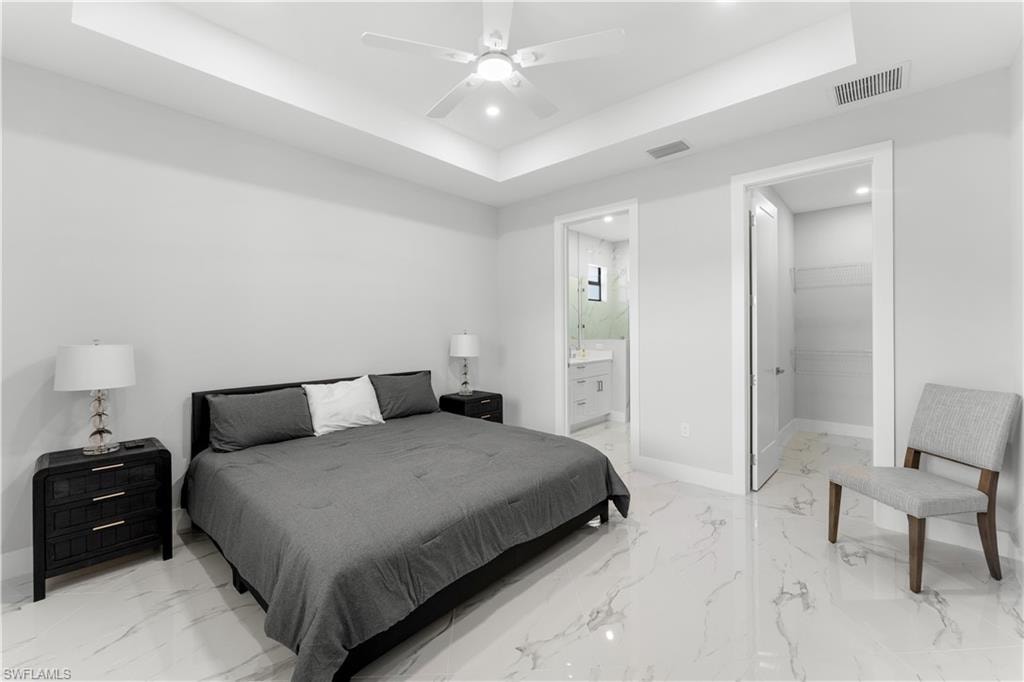 Spacious bedroom featuring large format tile flooring, a tray ceiling with recessed lighting, and a ceiling fan