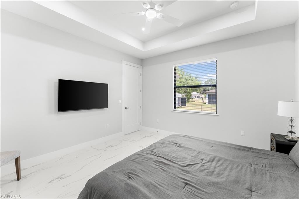 Spacious room featuring tray ceilings, a ceiling fan with integrated lighting, and white marble-look flooring