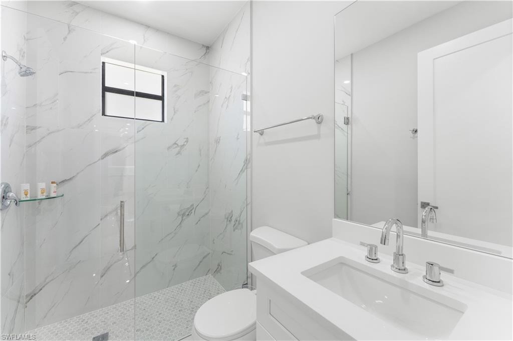 Modern bathroom featuring a glass-enclosed shower with large format tile walls and a mosaic tile floor, a window with black trim, a vanity with an integrated sink and chrome fixtures, and a frameless mirror