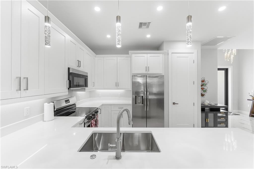 Modern kitchen featuring white shaker cabinetry, stainless steel appliances, a double basin stainless steel sink, quartz countertops, and recessed lighting with decorative pendant fixtures