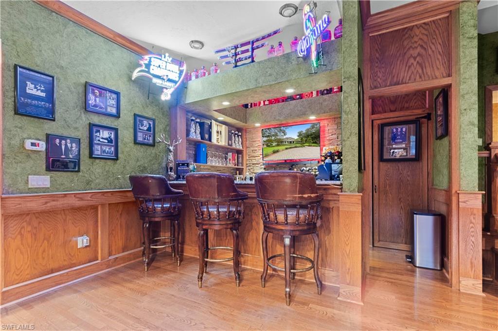 Custom bar area featuring hardwood flooring, wood wainscoting, and built-in shelving