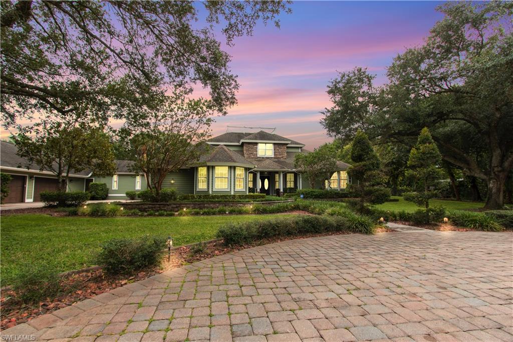 Expansive paver driveway leading to a two-story home with a stone and siding exterior