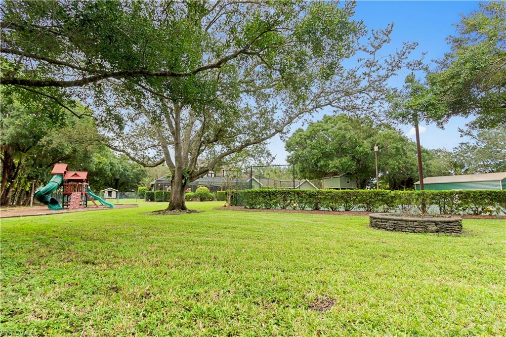 Expansive grassy area featuring mature trees, a stone-lined planter, and a dense hedge boundary