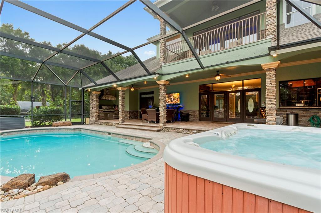 Screened outdoor living area featuring a built-in swimming pool, integrated spa, and an expansive patio paved with interlocking pavers