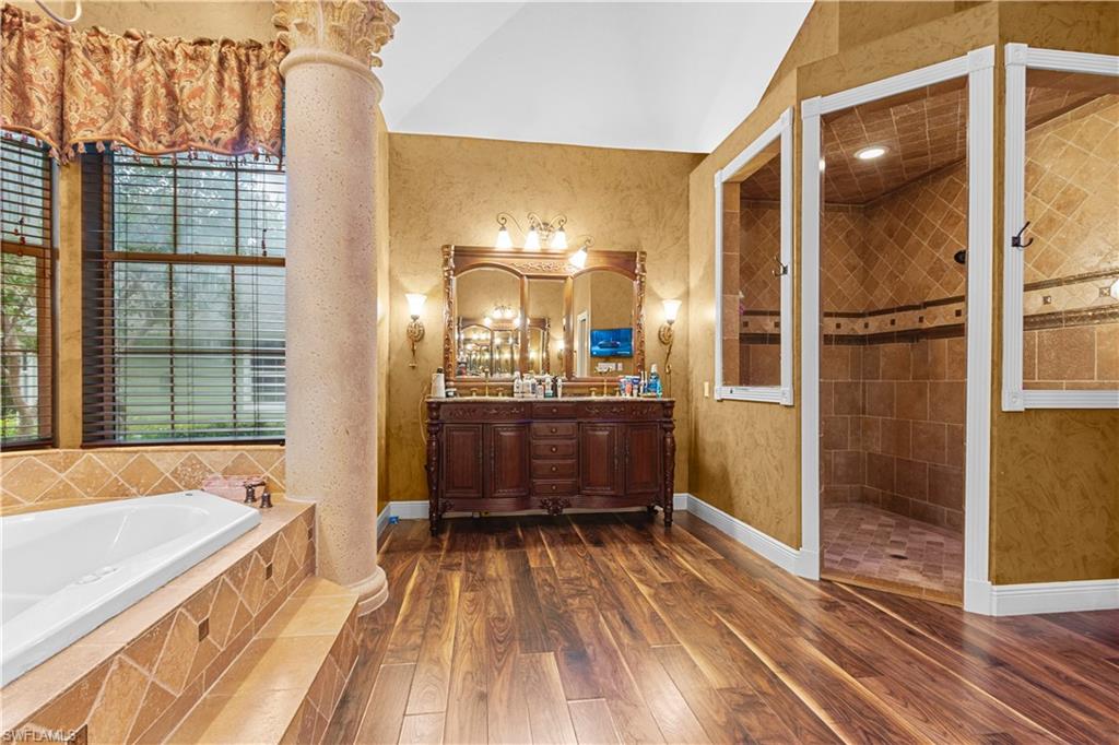Bathroom featuring wood-finish flooring, a freestanding soaking tub with tile surround, and a walk-in shower with tile walls and flooring