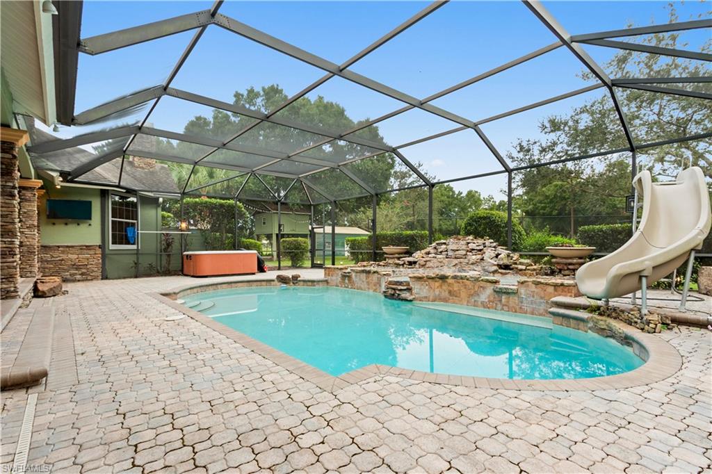 Screened outdoor living area featuring a freeform pool with a rock waterfall and slide