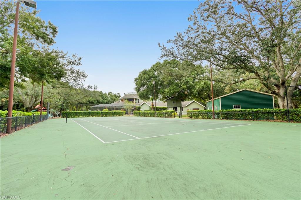 Tennis court featuring a green playing surface, perimeter fencing, and mature trees