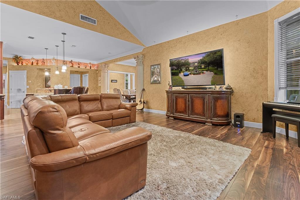 Spacious living area featuring high vaulted ceilings, rich wood-finish flooring, a wall-mounted television, and a built-in media console
