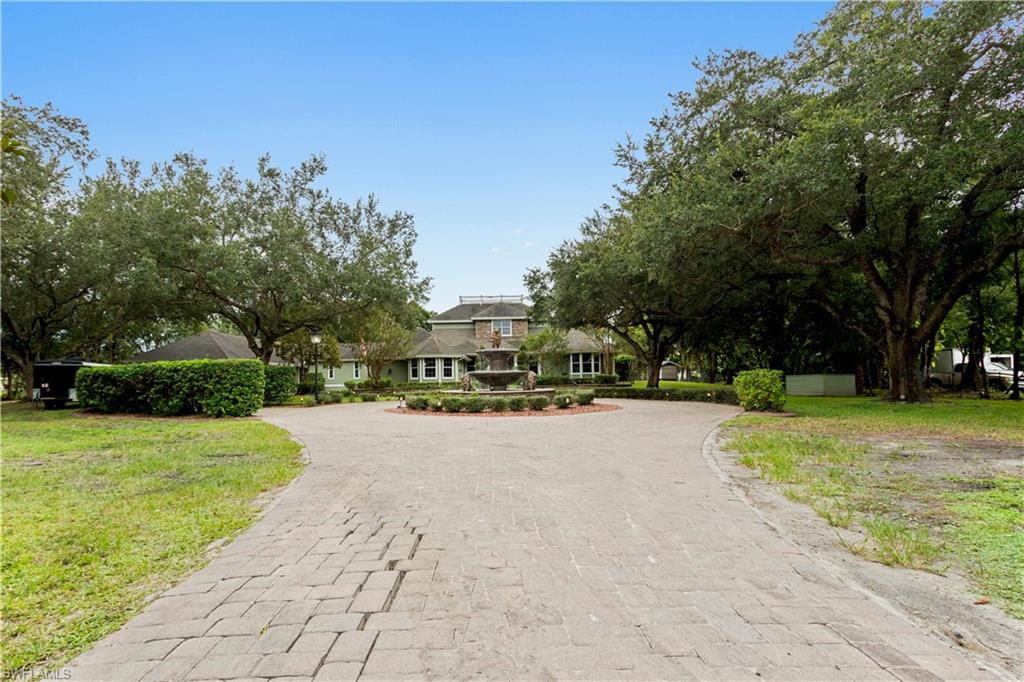 Expansive paver driveway with a central water feature, framed by mature trees