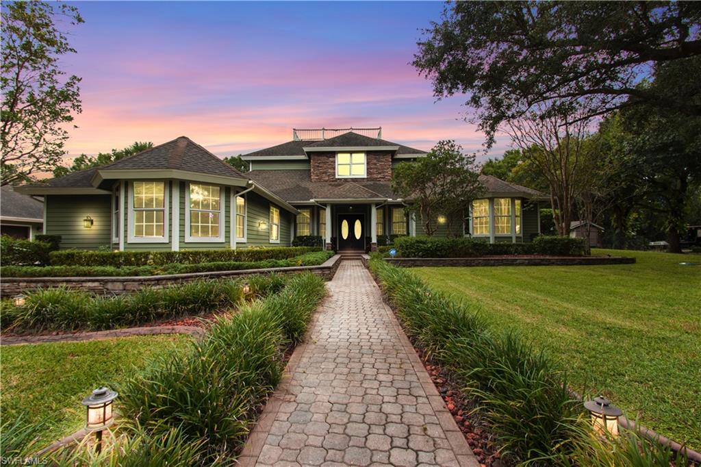 Expansive exterior featuring a paver walkway, mature landscaping, and a two-story design