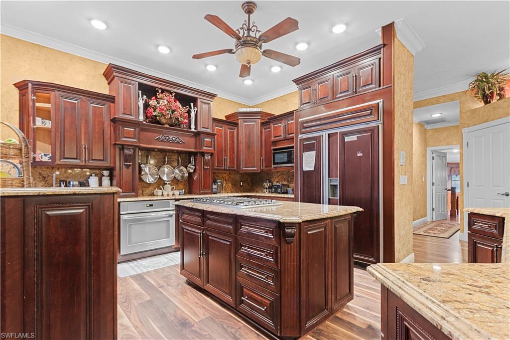 Gourmet kitchen featuring rich wood cabinetry, granite countertops, a central island with a built-in gas cooktop, recessed lighting, and wood-finish flooring