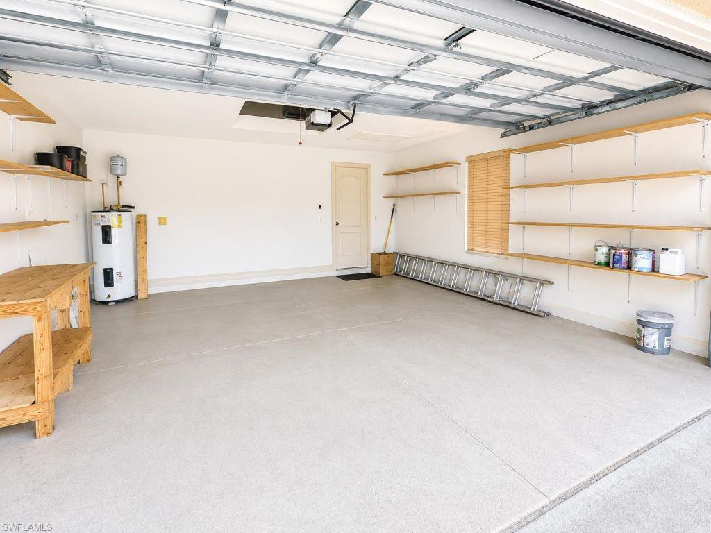 Spacious garage featuring a light-colored concrete floor, extensive built-in shelving, a workbench, and a ceiling-mounted garage door opener system