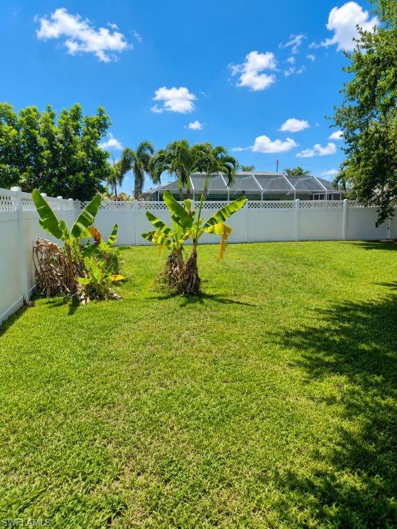 Expansive backyard featuring a green lawn, mature trees, and a white privacy fence