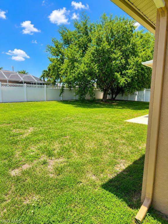 Spacious backyard featuring a large tree, green lawn, and white privacy fencing