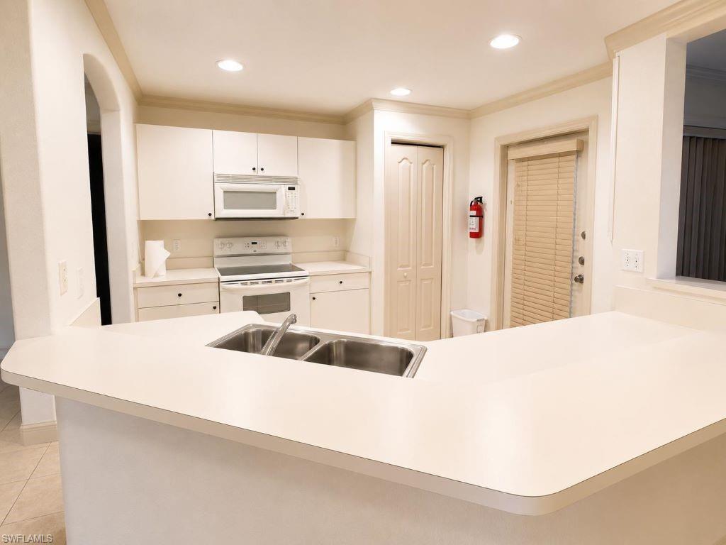 Kitchen featuring an integrated breakfast bar with a double basin sink, white cabinetry with dark hardware, recessed lighting, and a full suite of white appliances including a range and microwave