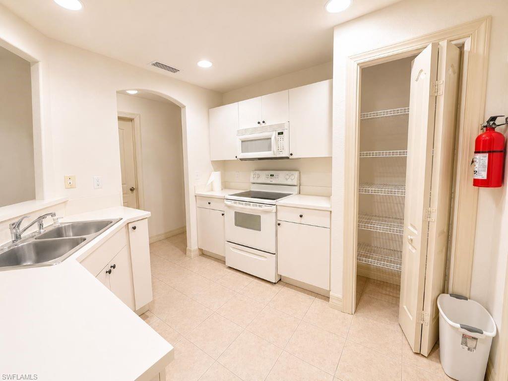 Neutral-toned kitchen featuring white cabinetry, a built-in microwave, a double-basin stainless steel sink, and a pantry with wire shelving