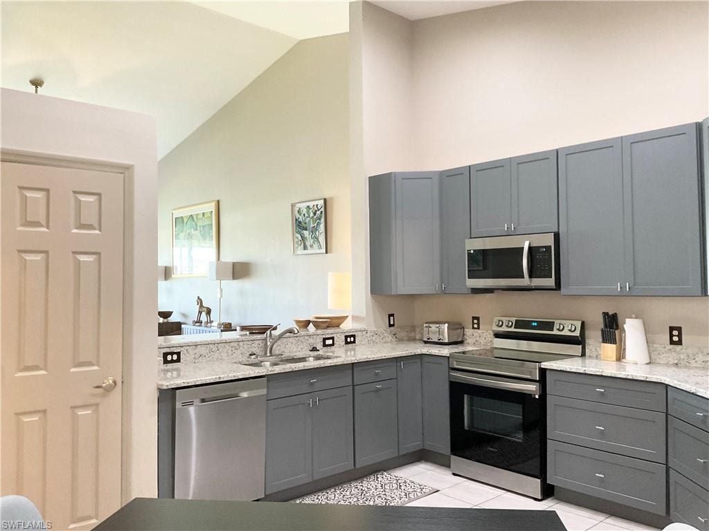 Kitchen featuring high vaulted ceiling, appliances with stainless steel finishes, sink, gray cabinetry and pantry.