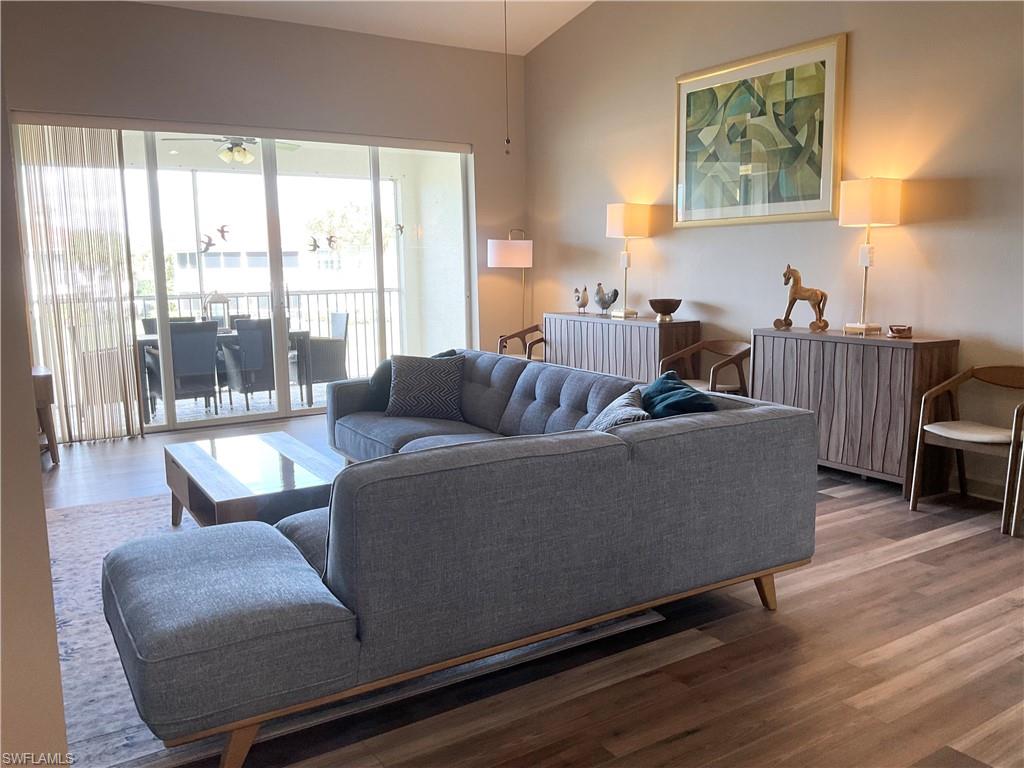 Living room with laminate wood-style floors, ceiling fan, and vaulted ceiling. Slider open to screened-in lanai