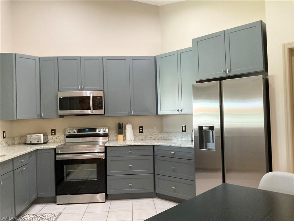 Kitchen with light stone countertops, light tile patterned floors, appliances with stainless steel finishes, and gray cabinets