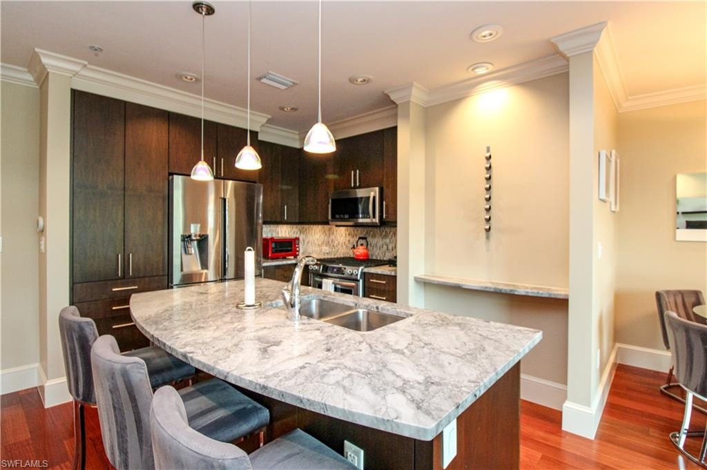 Kitchen featuring dark brown cabinets, stainless steel appliances, sink, hanging light fixtures, and a center island with sink