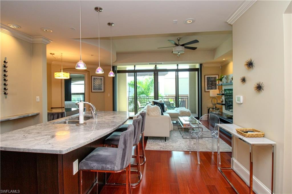 Kitchen with a breakfast bar area, dark hardwood / wood-style flooring, hanging light fixtures, ornamental molding, and ceiling fan