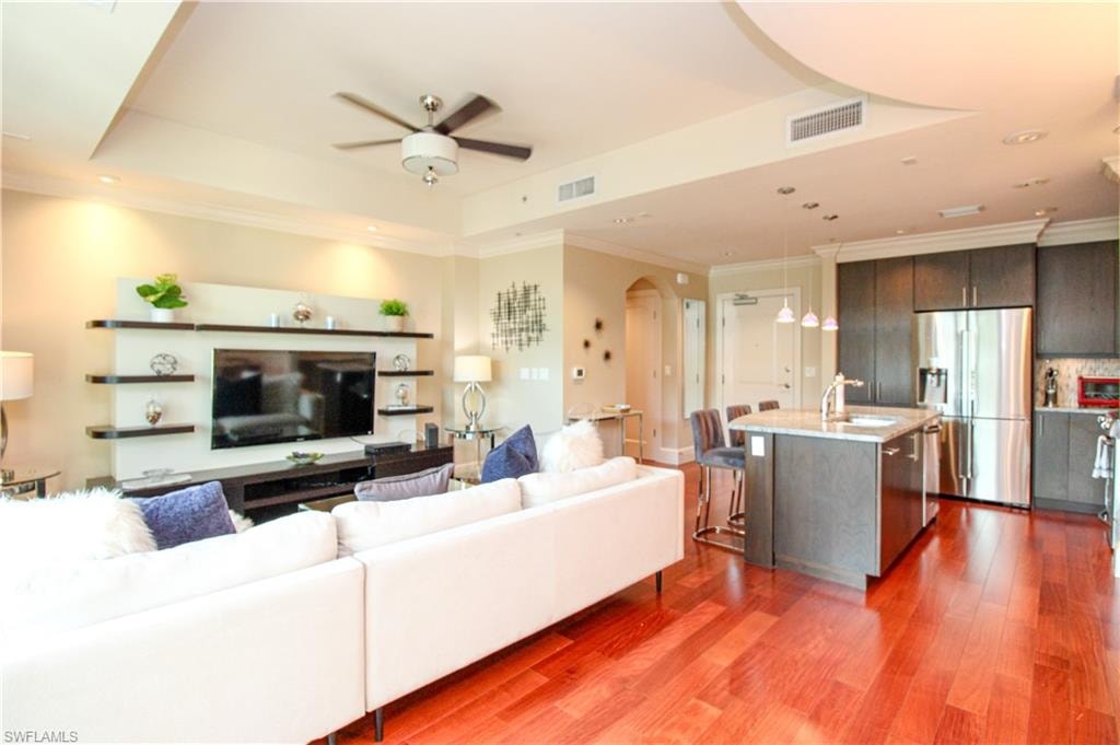 Living room with hardwood / wood-style floors, ceiling fan, a raised ceiling, and sink