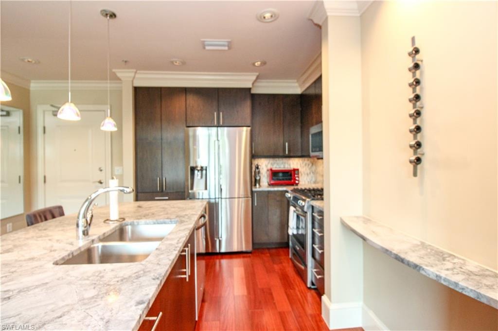 Kitchen featuring dark hardwood / wood-style floors, pendant lighting, appliances with stainless steel finishes, ornamental molding, and sink