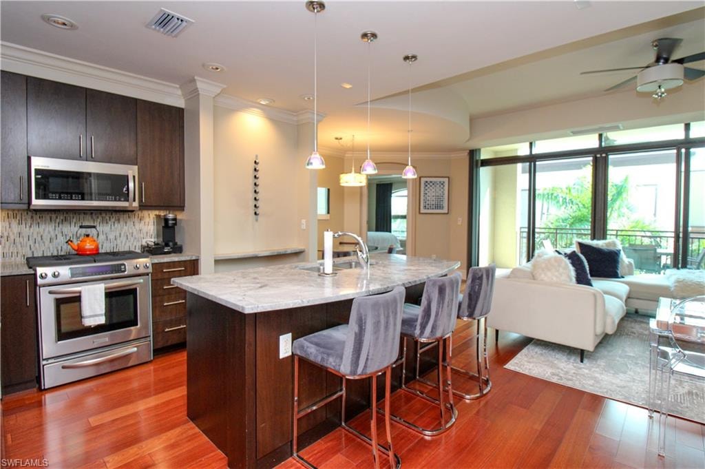 Kitchen with light hardwood / wood-style flooring, appliances with stainless steel finishes, an island with sink, pendant lighting, and a breakfast bar
