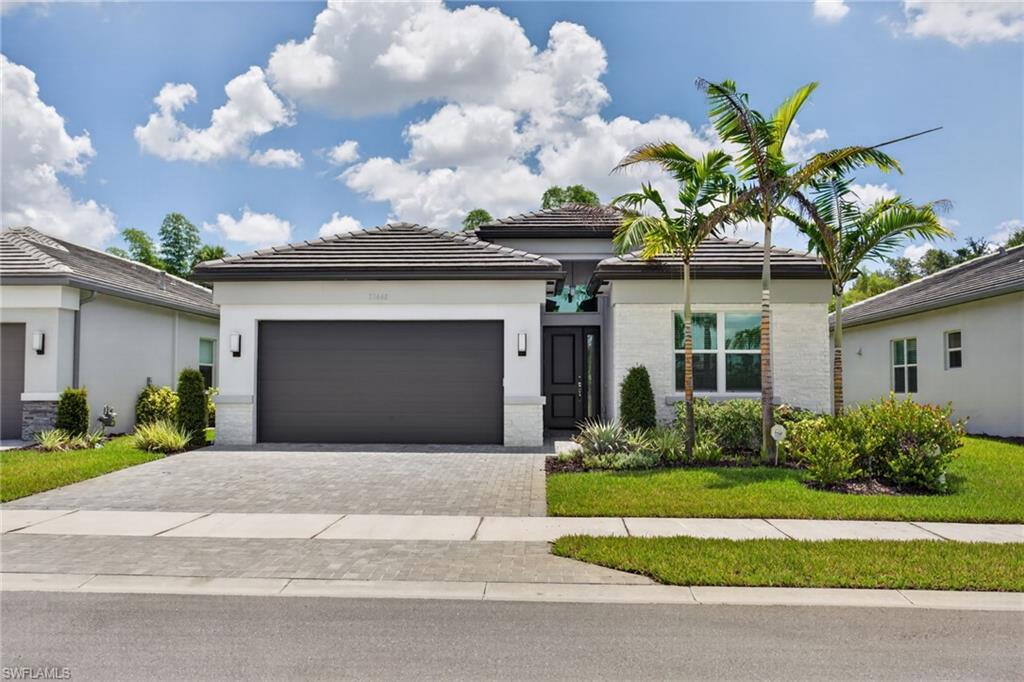 Contemporary single-story residence featuring a paver driveway, dark garage door, and a textured stucco facade with stone accents