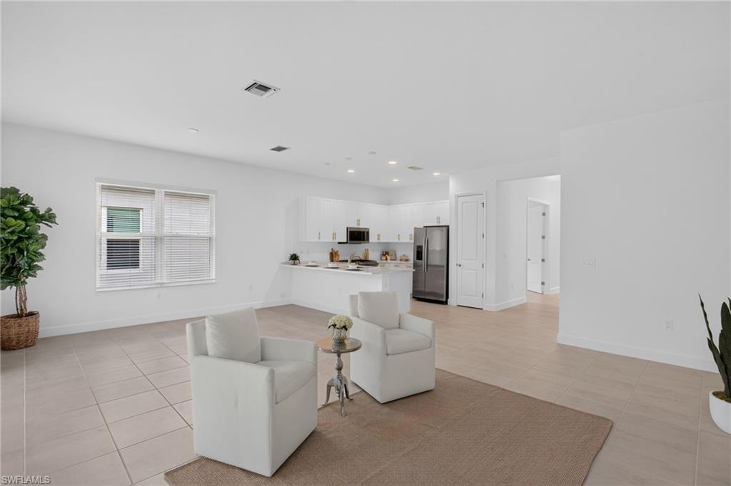 Open concept living space featuring neutral-toned tile flooring, a modern kitchen with white cabinetry, stainless steel appliances, and recessed lighting