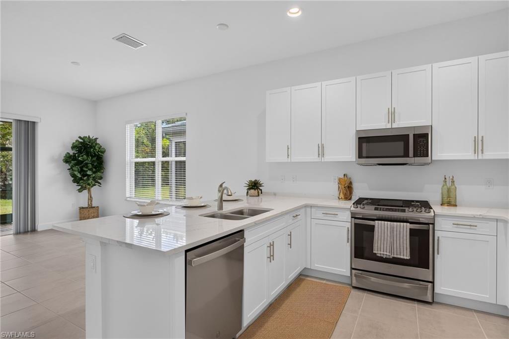 Modern kitchen featuring white shaker cabinetry with brushed gold hardware, stainless steel appliances, and light-toned countertops