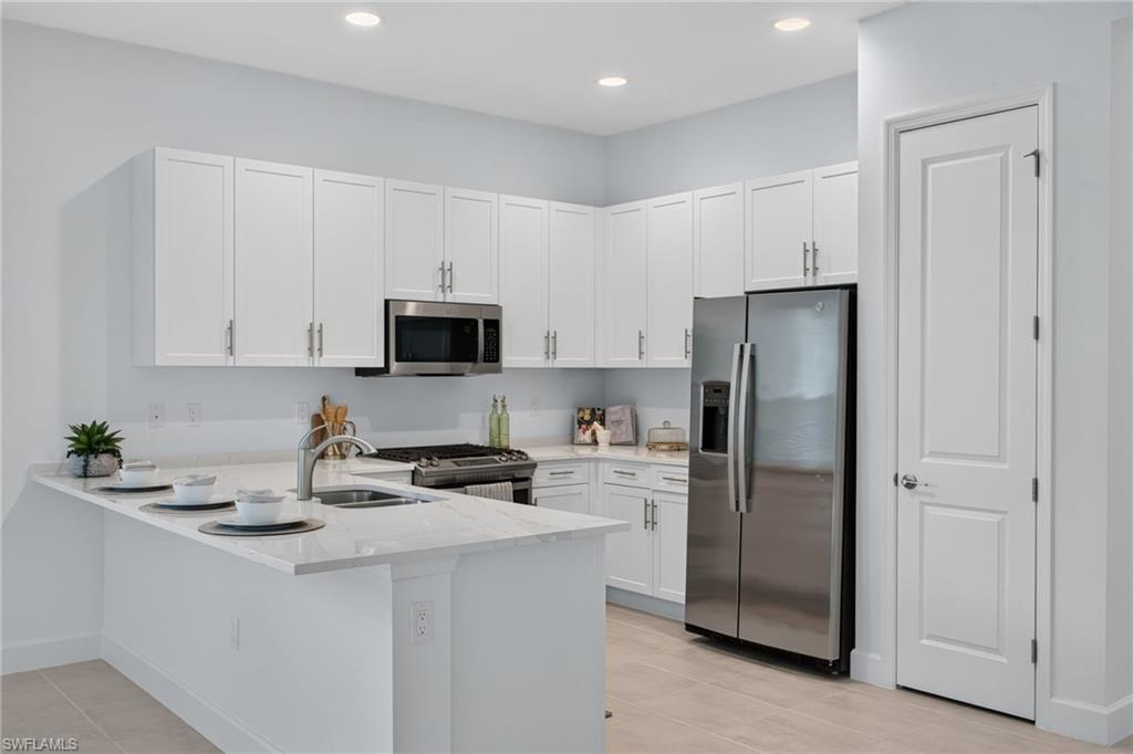 Modern kitchen featuring white cabinetry, light-toned countertops, stainless steel appliances, and recessed lighting