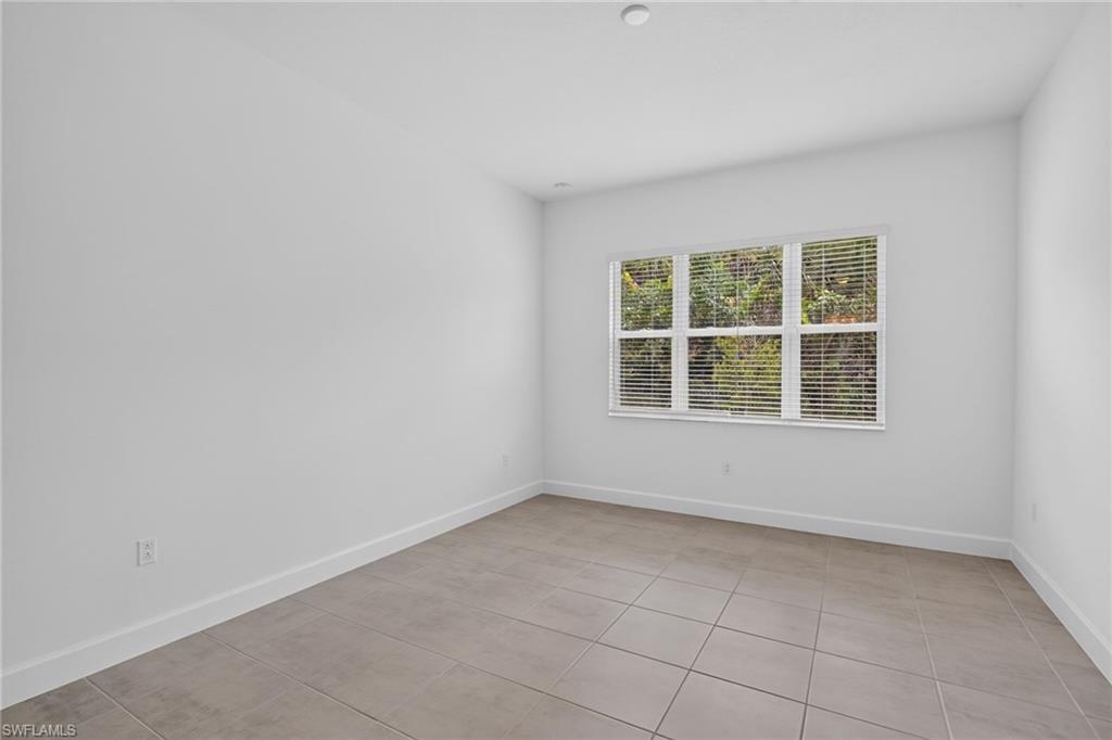 Spacious room featuring neutral tile flooring, white walls, and a large window with white blinds