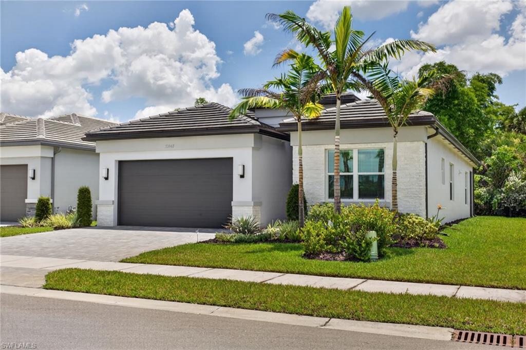 Modern stucco exterior with a dark tile roof, paver driveway, and an integrated two-car garage