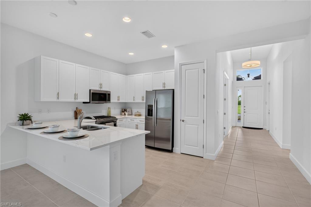 Modern kitchen featuring white shaker cabinetry, stainless steel appliances, a white stone island with an undermount sink, and recessed lighting