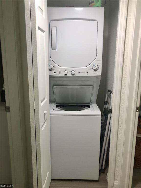 Dedicated laundry closet featuring a white stacked washer and dryer unit, bi-fold closet doors, and wood-finish flooring
