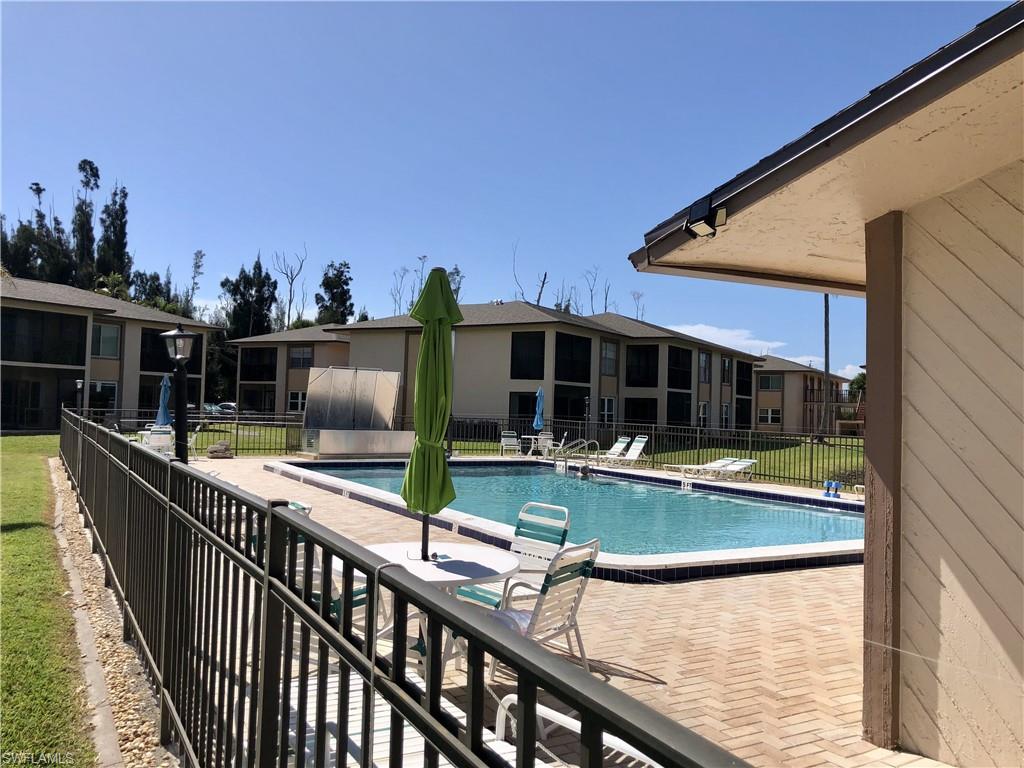 Community swimming pool featuring a brick paver surround, multiple lounge chairs, and a metal fence enclosure