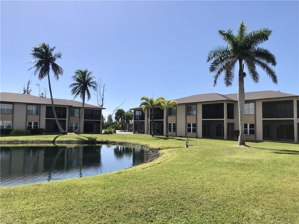Lush green lawn surrounding a tranquil pond, featuring multiple palm trees and low-rise buildings with screened-in balconies