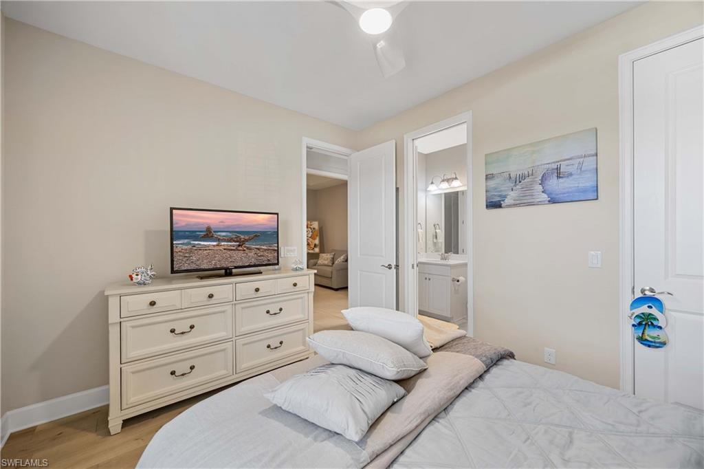 Bedroom with light wood finished floors, ensuite bathroom, and a ceiling fan