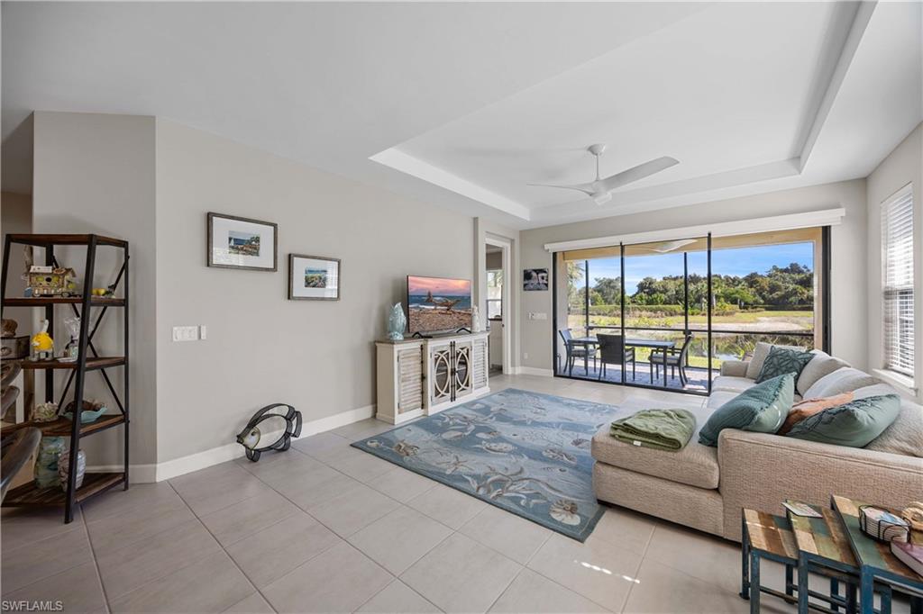 Living area featuring a tray ceiling, light tile patterned flooring, ceiling fan, and a sunroom