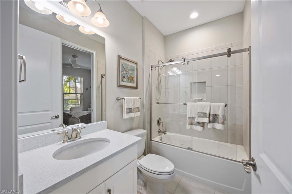 Ensuite bathroom with bath / shower combo with glass door, vanity, and light tile patterned floors