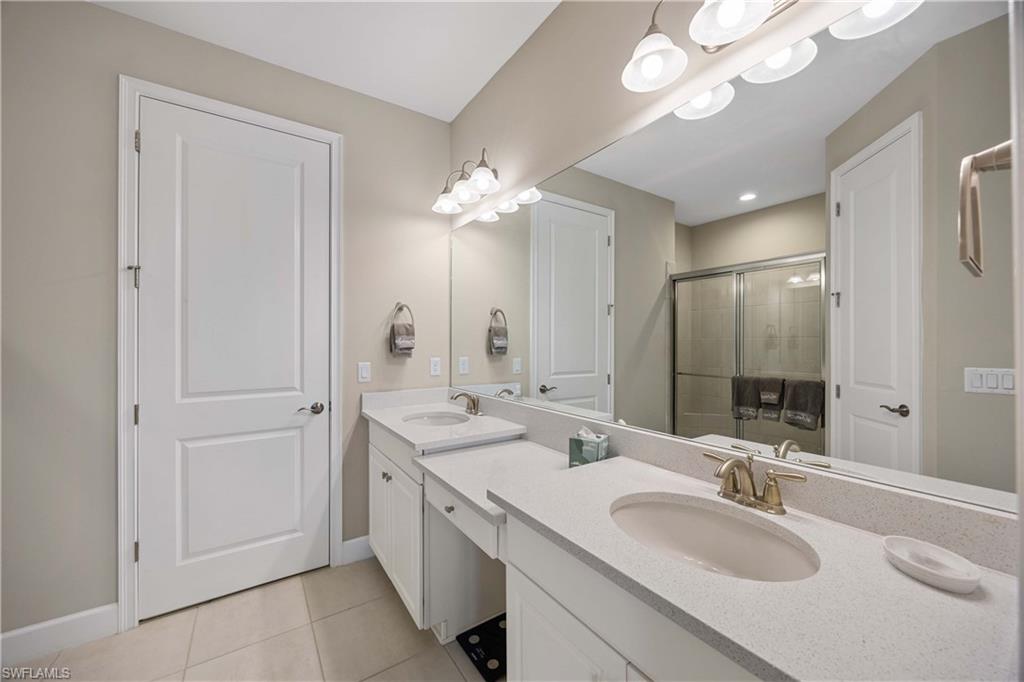 Bathroom with double vanity, light tile patterned floors, and a shower stall