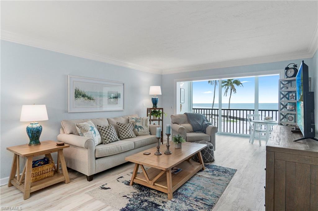 Living area featuring expansive sliding glass doors, white crown molding, light-toned wood-finish flooring, and a balcony overlooking the ocean