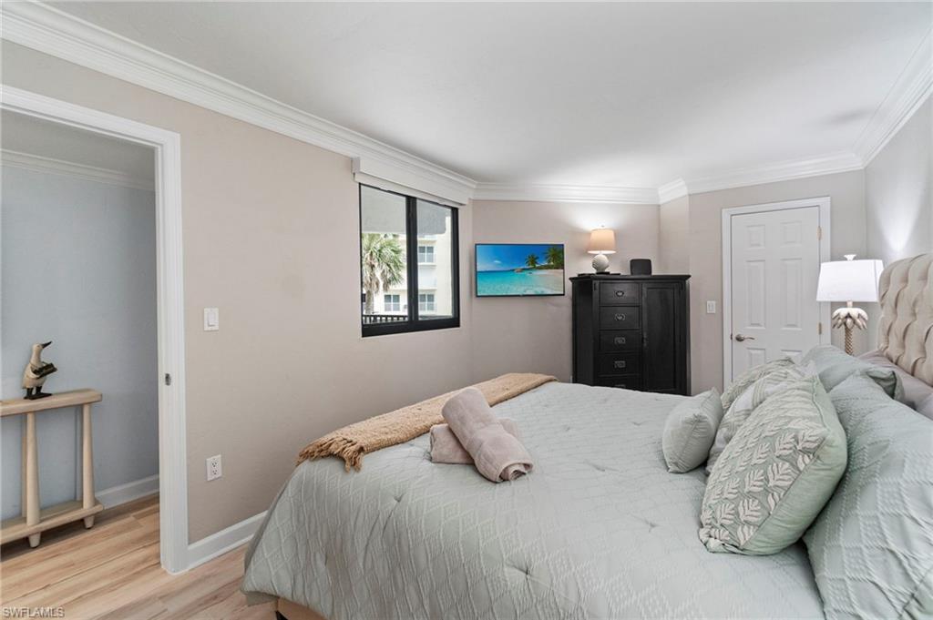 Light-filled room featuring crown molding, neutral wall tones, wood-finish flooring, a window with exterior views, and a paneled door