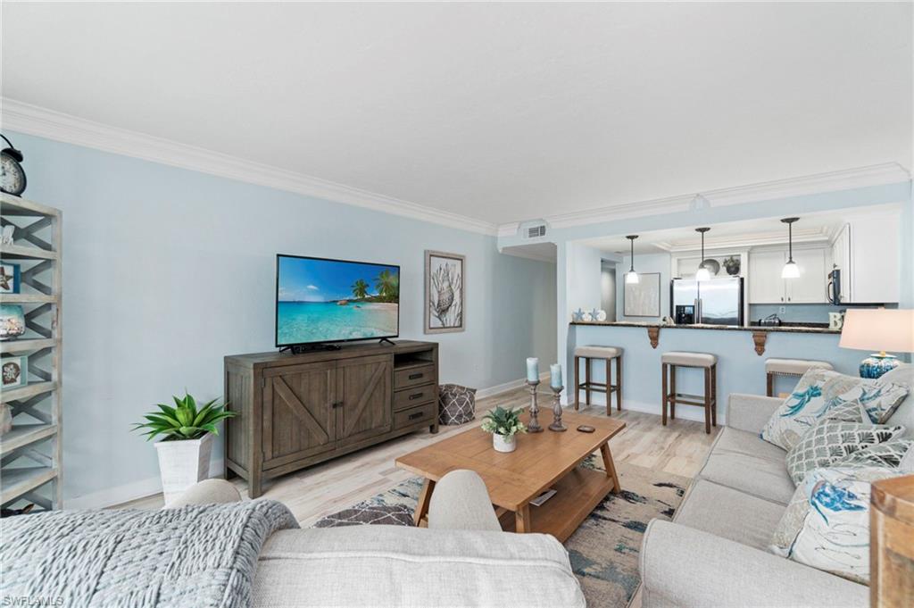 Open-concept living area featuring light wood-finish flooring, crown molding, and a built-in breakfast bar with pendant lighting