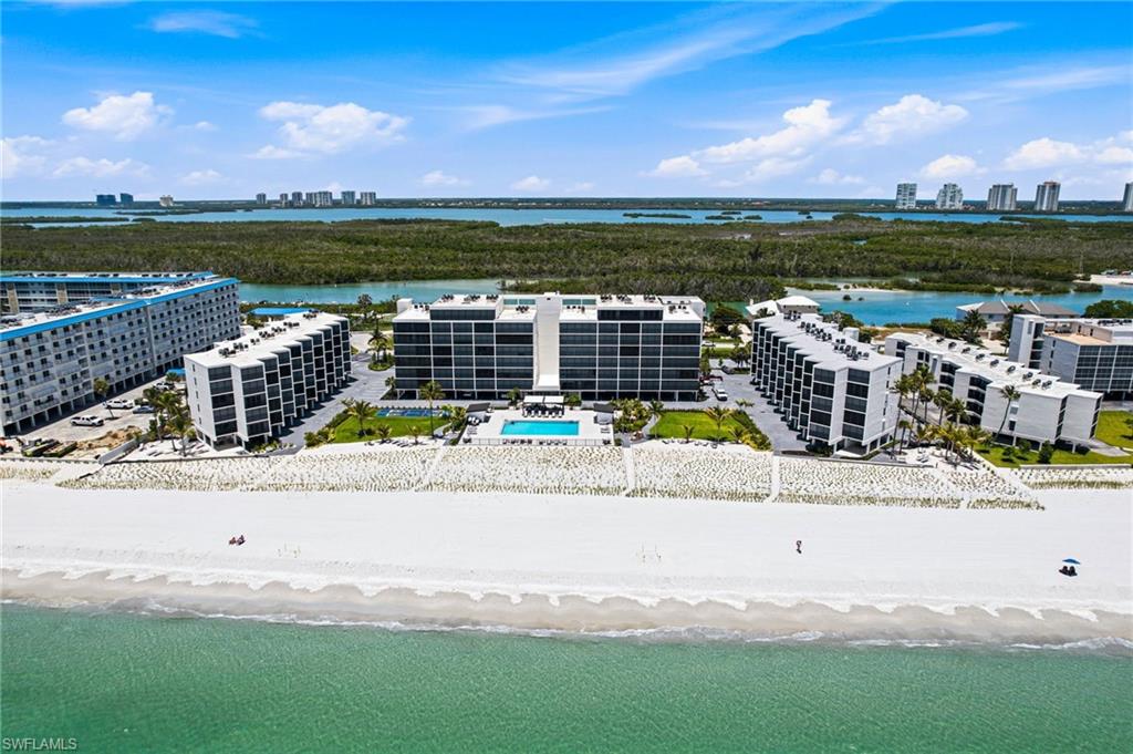 Coastal condominiums featuring multiple buildings with private balconies, direct beach access, an outdoor swimming pool, and manicured landscaping