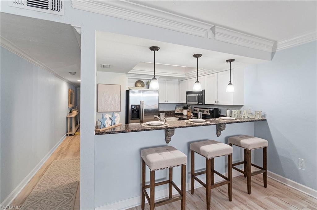 Kitchen featuring white cabinetry, stainless steel appliances, a dark stone countertop, and a breakfast bar with three pendant lights