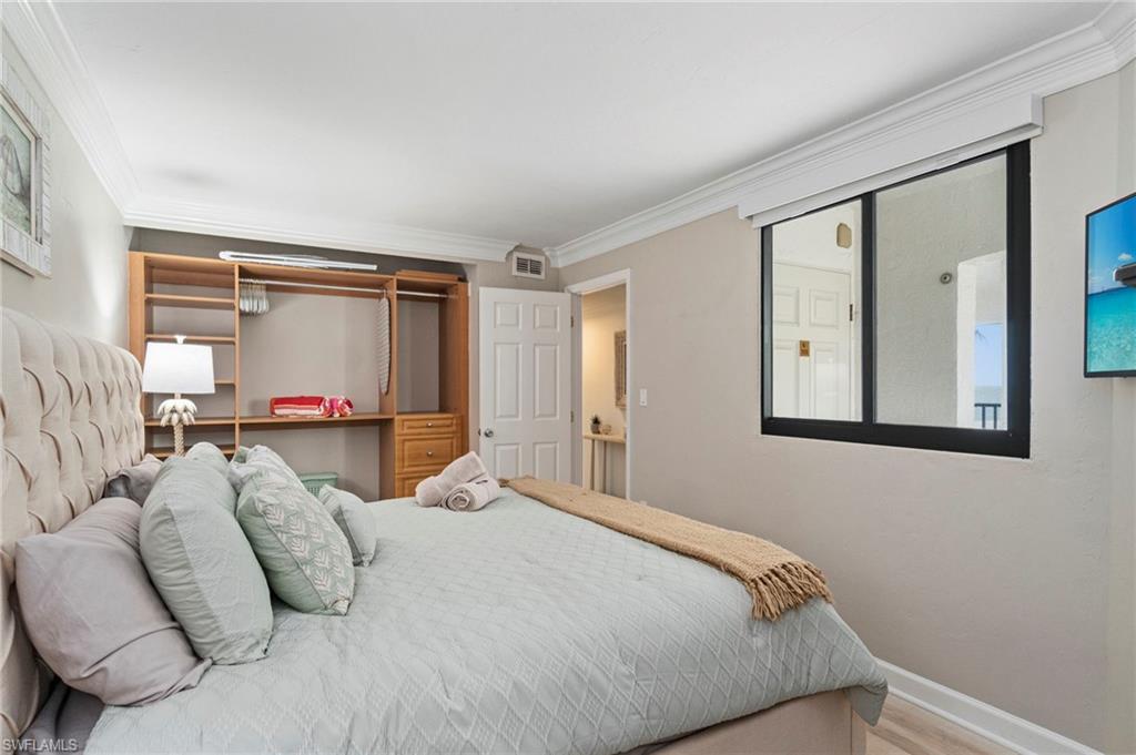 Bedroom featuring a built-in wood-finish closet system with shelving and hanging space, crown molding, and light wood-finish flooring