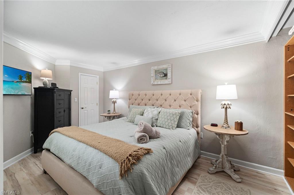 Spacious bedroom featuring light wood-finish flooring, crown molding, and a paneled door